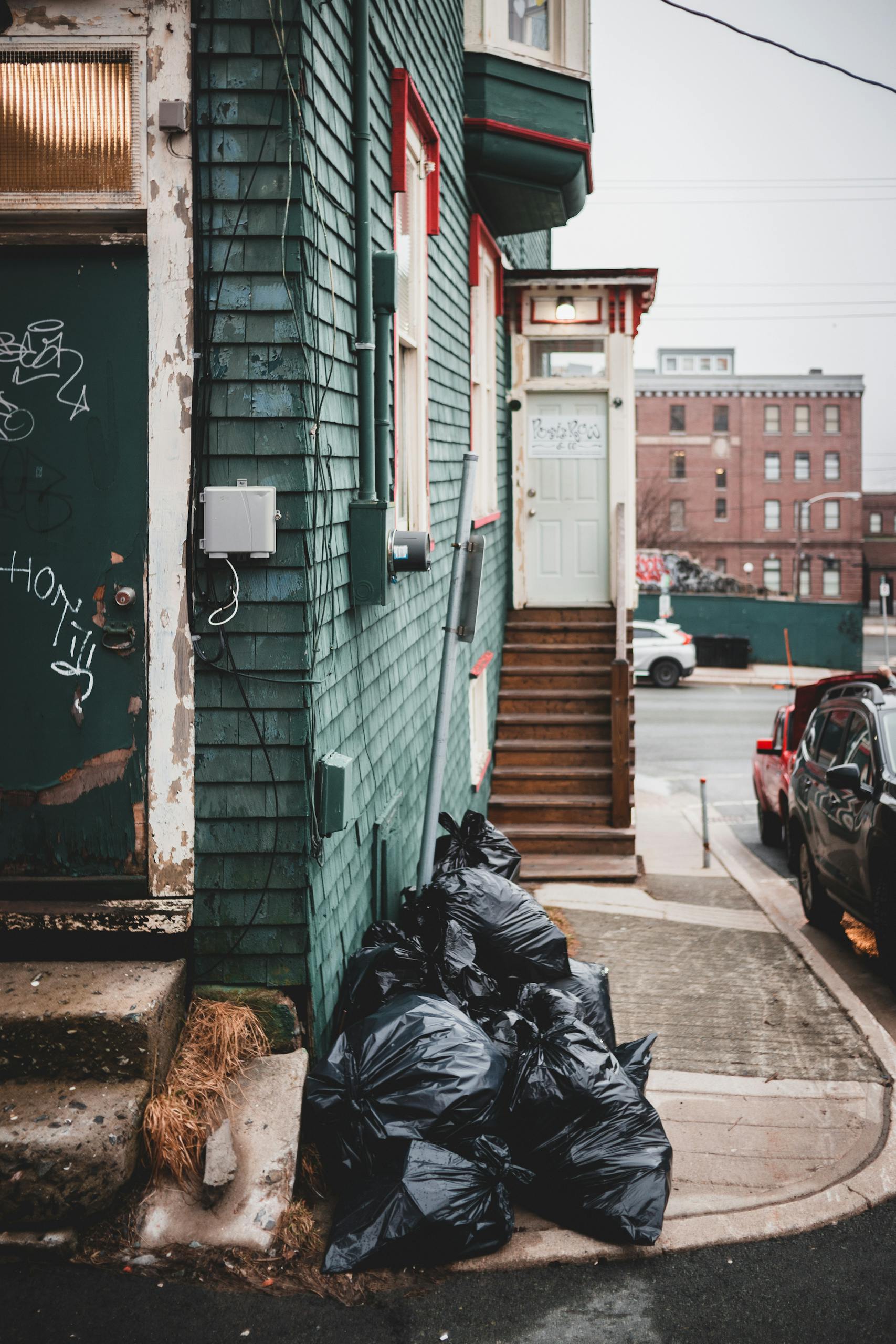 City alley with trash bags and graffiti, highlighting urban pollution issues.